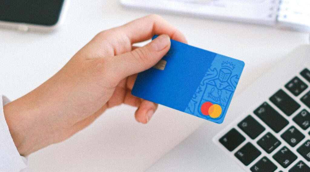 a hand holding a blue credit card, about to pay for something online.